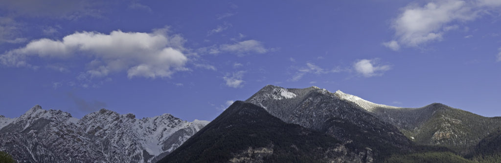 Panorama of wooded and snowy mountains, with blue sky and clouds